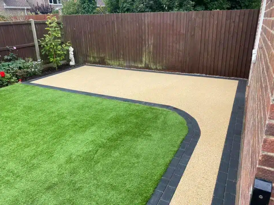 Artificial grass lawn with resin bound patio and black block edging in a landscaped garden.