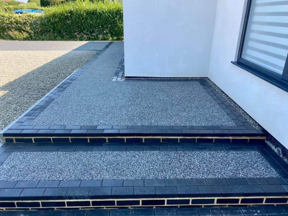 Resin driveway with black brick edging and steps leading to modern home entrance